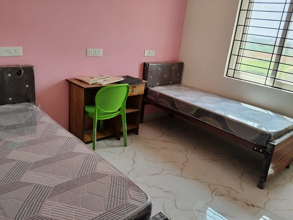 Two beds and a wooden desk beside a window in a pink and white room.